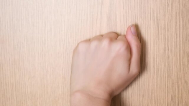Close-up of a clenched fist knocking firmly on a closed wooden door. Persistent knocking conveys urgency, determination, request for attention and communication