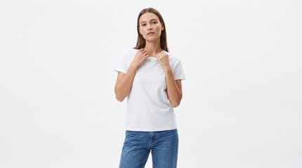 Obraz premium A young woman with long brown hair poses gracefully while wearing a classic white t-shirt and blue denim jeans against a plain backdrop