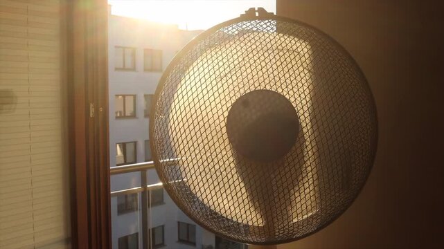 An electric fan standing inside a room at sunrise on a hot summer morning, circulating cool air to improve ventilation during an extreme heatwave.