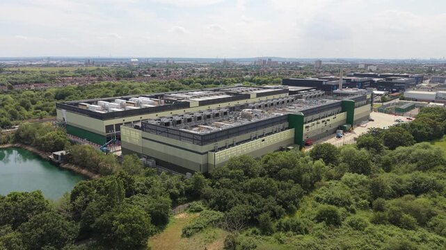 Aerial view of a large data center facility with rooftop cooling units, surrounded by lush green trees and a small pond in London, London, United Kingdom.