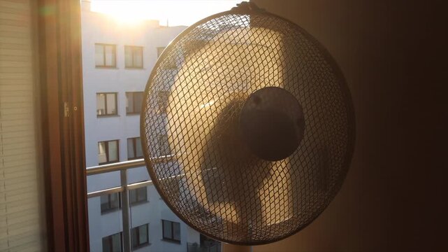 An electric fan standing inside a room at sunrise on a hot summer morning, circulating cool air to improve ventilation during an extreme heatwave.