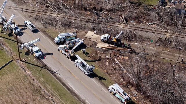 Aerial drone view of utility crews repairing damaged power lines after a severe storm or tornado. Bucket trucks and electrical workers restoring the power grid in a disaster affected area with fallen 