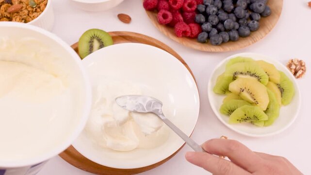 Spoon Scooping Fresh Greek Yogurt Into White Bowl For Breakfast Preparation
