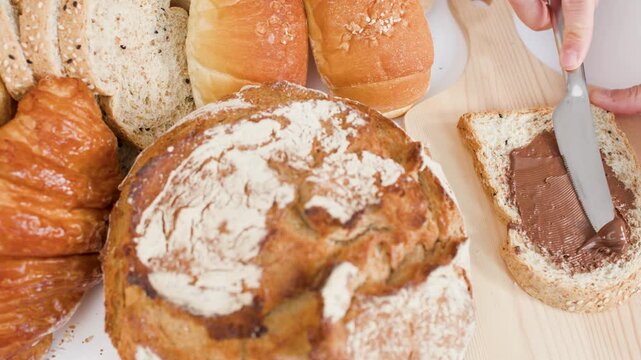 Spreading Chocolate Hazelnut Cream on Fresh Sliced Bread with Bakery Assortment