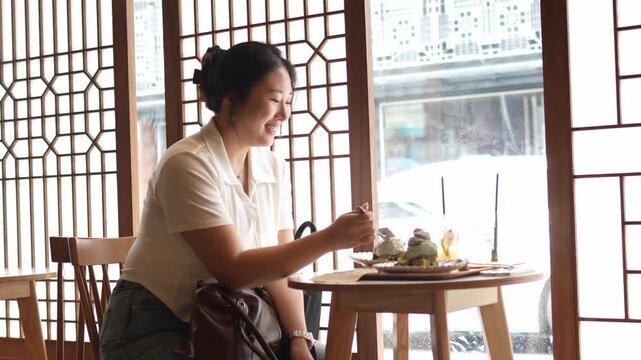Woman sips tea at traditional cafe window. Soft light filters through patterned wooden screens. She smiles gently, content and relaxed. Perfect for tranquil cafe or cultural scene projects