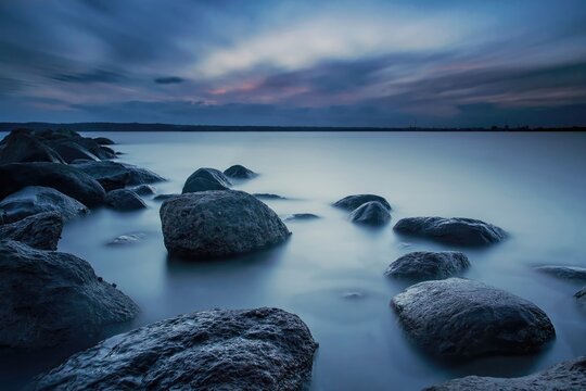 Calm ocean with rocks under colorful sky at sunset