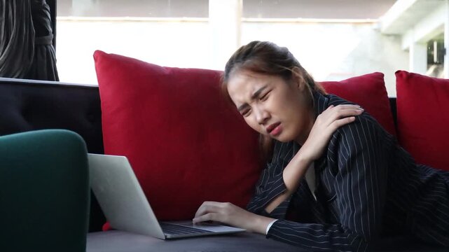 young adult asian businesswoman feeling uncomfortable with stiff shoulders and fatigue after prolonged sitting on couch with bad working posture
