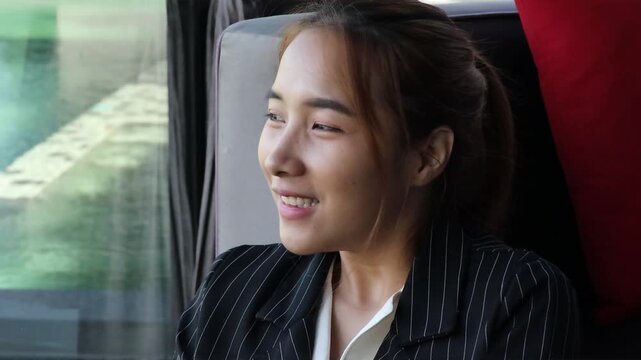 relaxed young asian businesswoman looking out window at urban pond during daytime break, feeling calm and refreshed after work stress