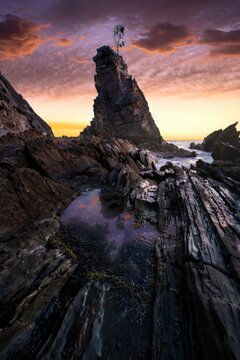 Cliff with lighthouse at sunset with colorful sky and rocks
