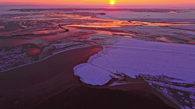 Aerial drone footage of partially frozen lake at golden sunset with snow covered village outskirts, rural Romania, winter