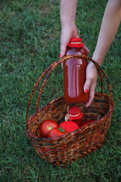 Woman placing reusable glass bottle of homemade tomato juice into wicker basket with fresh tomatoes, farm to table concept