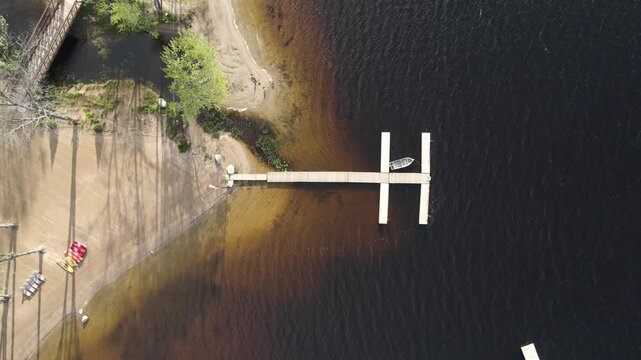 Aerial view of the wooden dock extending into the dark waters of Commanda Lake with a sandy shoreline and bridge in Restoule, Ontario, Canada.