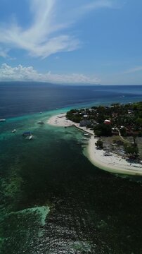 Vertical drone flies over Public Pamilacan Beach and tilts down toward white sand, coral reef, boats, and blue water in Bohol
