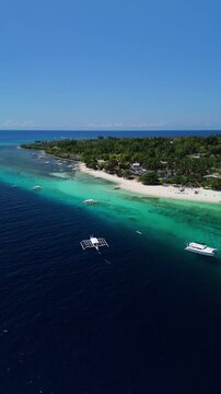Vertical drone tracks and orbits a boat approaching Public Pamilacan Beach, showing white sand, reef, and blue water in Bohol