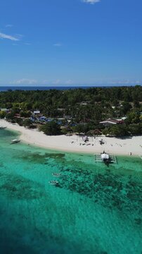 Vertical drone orbits and follows two kayakers beside Public Pamilacan Beach, showing white sand, reef, boats, and blue water