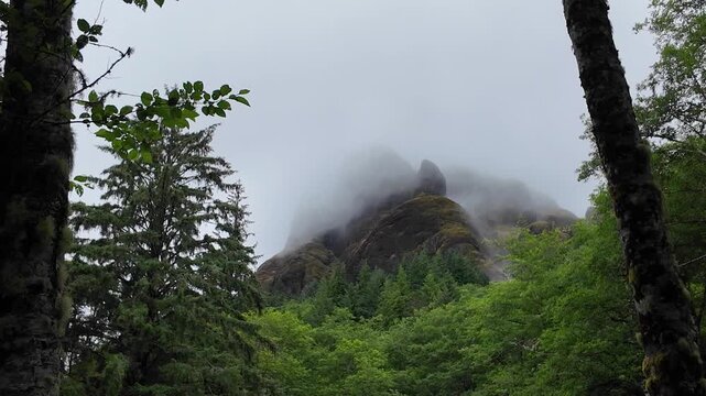 4K static action camera footage of low clouds and fog drifting across rocky cliffs near the summit of Saddle Mountain in Oregon's Coast Range, USA. Misty rainy Pacific Northwest landscape.