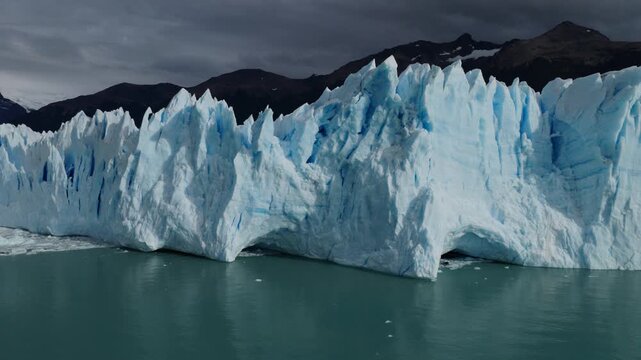 Perito Moreno Glacier in Los Glaciares National Park, Santa Cruz, Argentina, displays towering ice cliffs, compressed blue ice and active calving formations above Lago Argentino, drone lateral slide