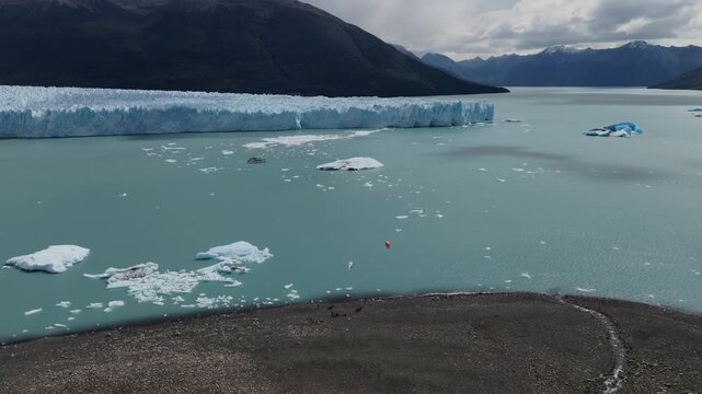 Kitesurfers on Lago Argentino near Perito Moreno Glacier, Santa Cruz, Argentina, with floating icebergs and Patagonian mountains, wide angle drone push in shot.