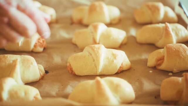 Close-up of baker hand touching and squeezing a hot baked crescent roll to check softness. Fresh homemade savory croissants straight from the oven on a baking tray with paper background, 4k.