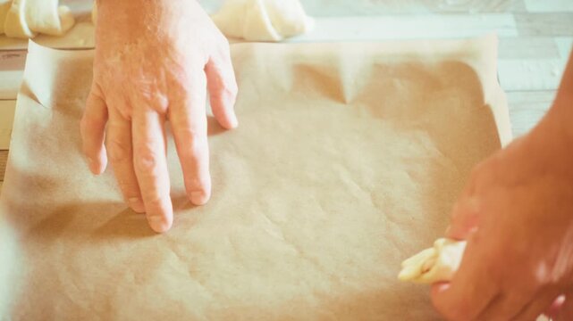 Close-up of chef hands placing raw stuffed crescent rolls onto a baking sheet with parchment paper. Preparing homemade savory pastry or croissants on kitchen table before oven baking, 4k.