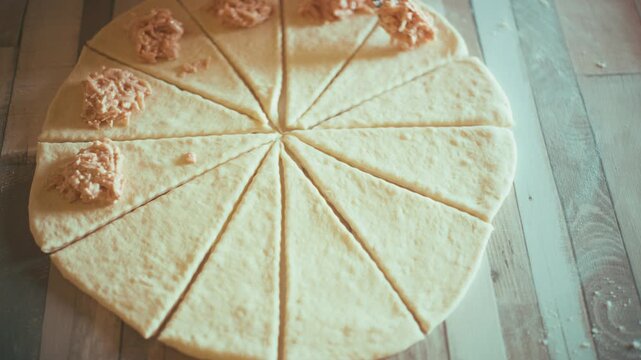 Close-up of chef hands adding homemade ham, cheese and tomato sauce filling onto sliced dough triangles. Preparing savory pastry rolls or stuffed croissants on a wooden kitchen table, 4k.