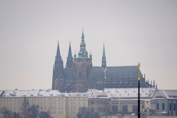 Obraz premium Magnificent historical castle complex featuring majestic gothic cathedral towers rises above snow covered palace buildings under a pale overcast winter sky, capturing a cold seasonal scene.