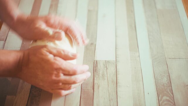 Close-up of chef hands kneading fresh raw dough directly on a wooden kitchen countertop. Authentic process of shaping homemade bread or pizza crust, traditional baking concept video, 4k.