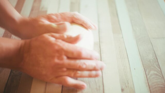 Close-up of chef hands kneading fresh raw dough directly on a wooden kitchen countertop. Authentic process of shaping homemade bread or pizza crust, traditional baking concept video, 4k.