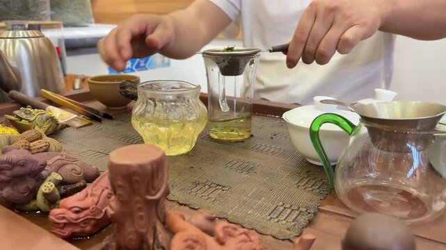 Close-up of a tea master pouring freshly brewed tea through a strainer into a glass cup during a traditional ceremony