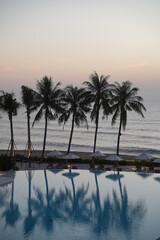 Obraz premium Tropical resort palm tree infinity pool ocean sunset reflection luxury vacation tranquil seaside with calm water and soft sky