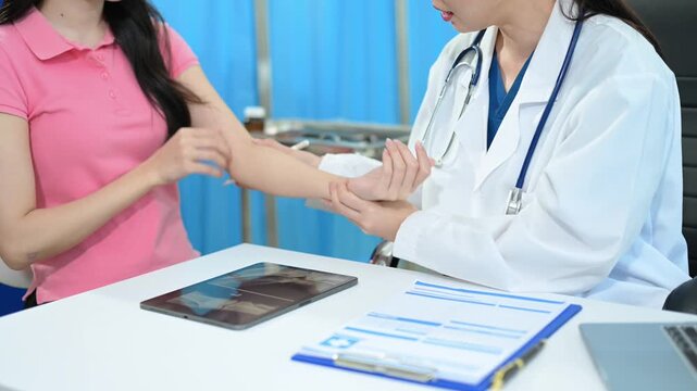 Asian female doctor examines a patient's injured arm and shows bone X-ray results on a laptop in a hospital room. Perfect for healthcare and orthopedics themes.