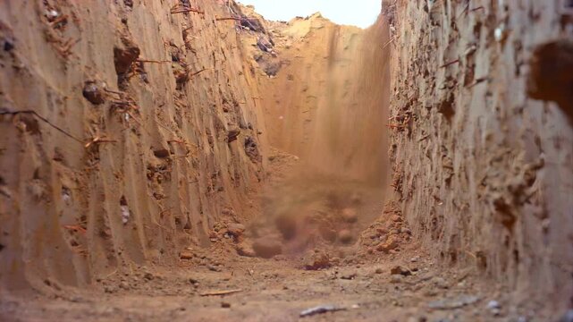 POV from inside narrow square excavation as metal shovel digs through compact soil walls, capturing grave-like trench construction, burial pit excavation, manual labor, underground earthwork activity.