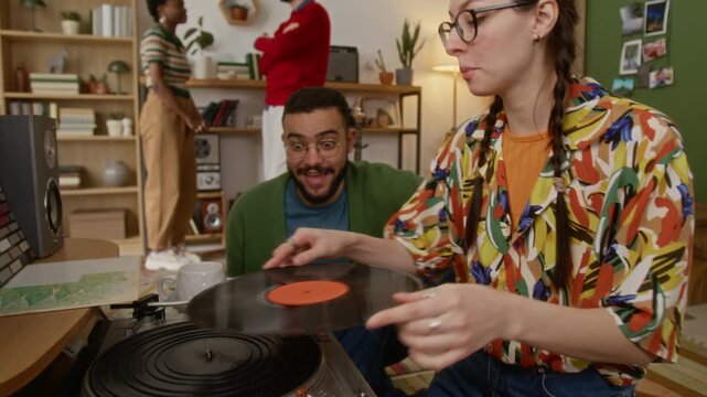 Close up shot of two friends discussing and playing vynyl record during homely party in cozy living room