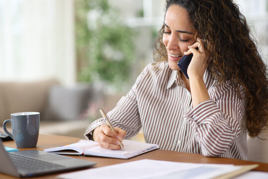 Happy adult teleworker writing in agenda and talking on phone