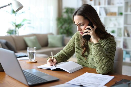 Worried teleworker talking on phone and taking notes