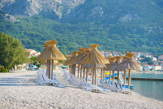 Traditional straw parasols lined up along the famous pebble beach in Ba&scaron;ka, with lush green hills and rocky mountains rising above the Adriatic coast