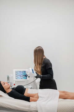 Female aesthetic practitioner performing a non‑invasive body treatment on clients abdominal area