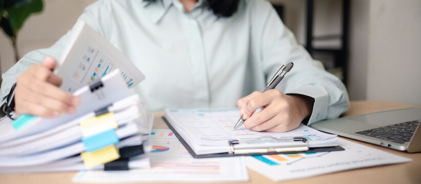 Business professional reviewing performance reports and auditing stack of documents at office desk. Concept of corporate audit, compliance check, data analysis,