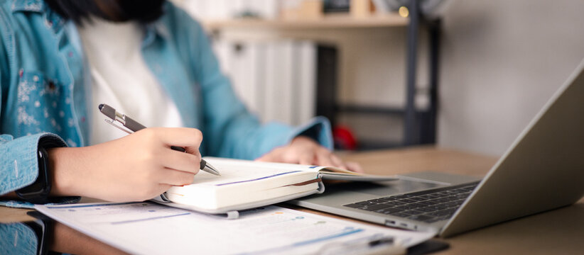 Professional planning workspace with hands writing notes on calendar, documents and laptop on desk, representing business planning, time management, productivity, organization,