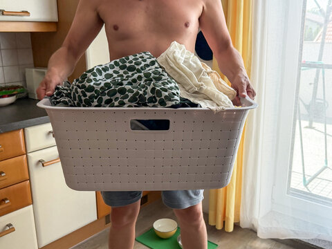 Ein Mann &uuml;ber 50 mit einem W&auml;schekorb voller Kleidung in einer K&uuml;che. Waschen, Hausarbeit, Zuhause. 