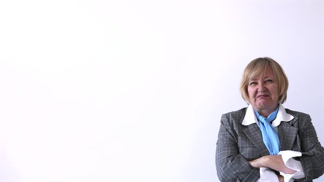 Senior Businesswoman Showing Disapproval with Arms Crossed. Senior businesswoman with crossed arms making a displeased and skeptical facial expression against a plain light background with copy space.