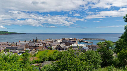 Naklejka premium The Harbour at Stonehaven lined with traditional stone buildings and a Clock Tower seen from the path to Black Hill.