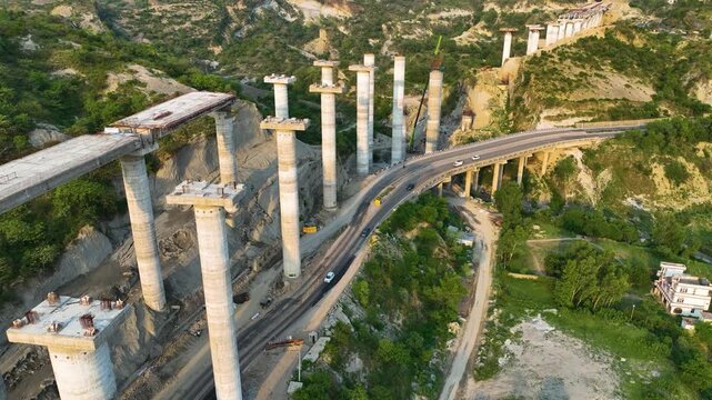 Drone shot of unfinished elevated highway viaduct and heavy bridge construction over existing road.