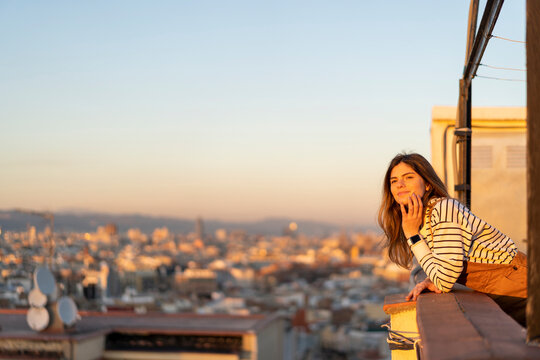 Portrait of content young woman relaxing on roof terrace at sunset