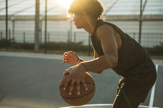 Athlete dribbling basketball in sports court at sunset