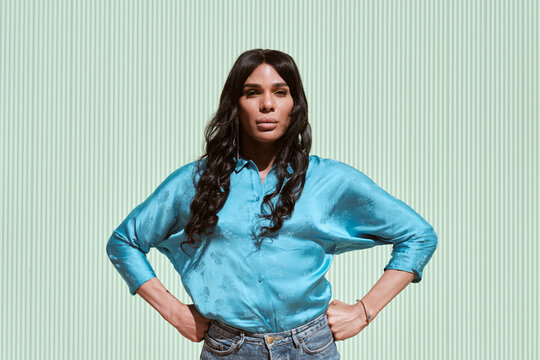 Fashionable non-binary woman standing with hands on hips in front of wall