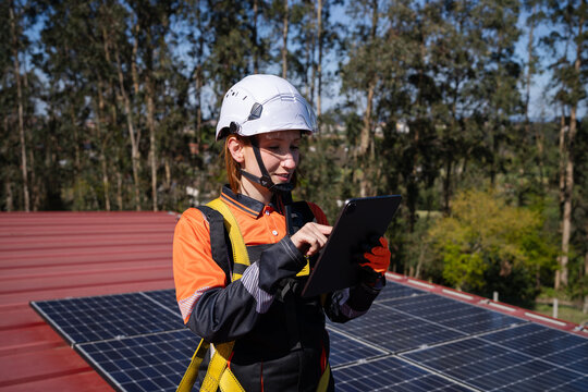 Technician inspecting solar panel on roof using tablet