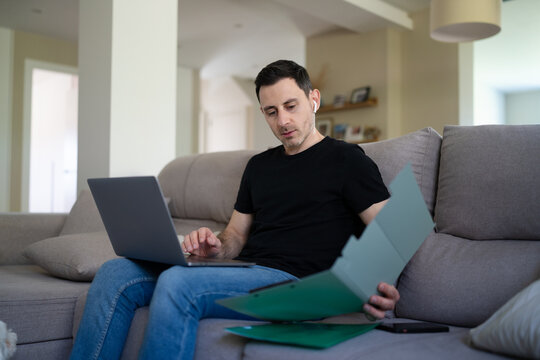 Freelancer working on laptop with documents on sofa at home