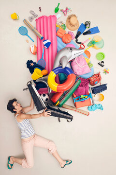 Woman struggling with overpacked suitcase and vacation items in studio