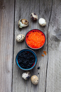 Black and red caviar in bowls, boiled quail eggs on wood
